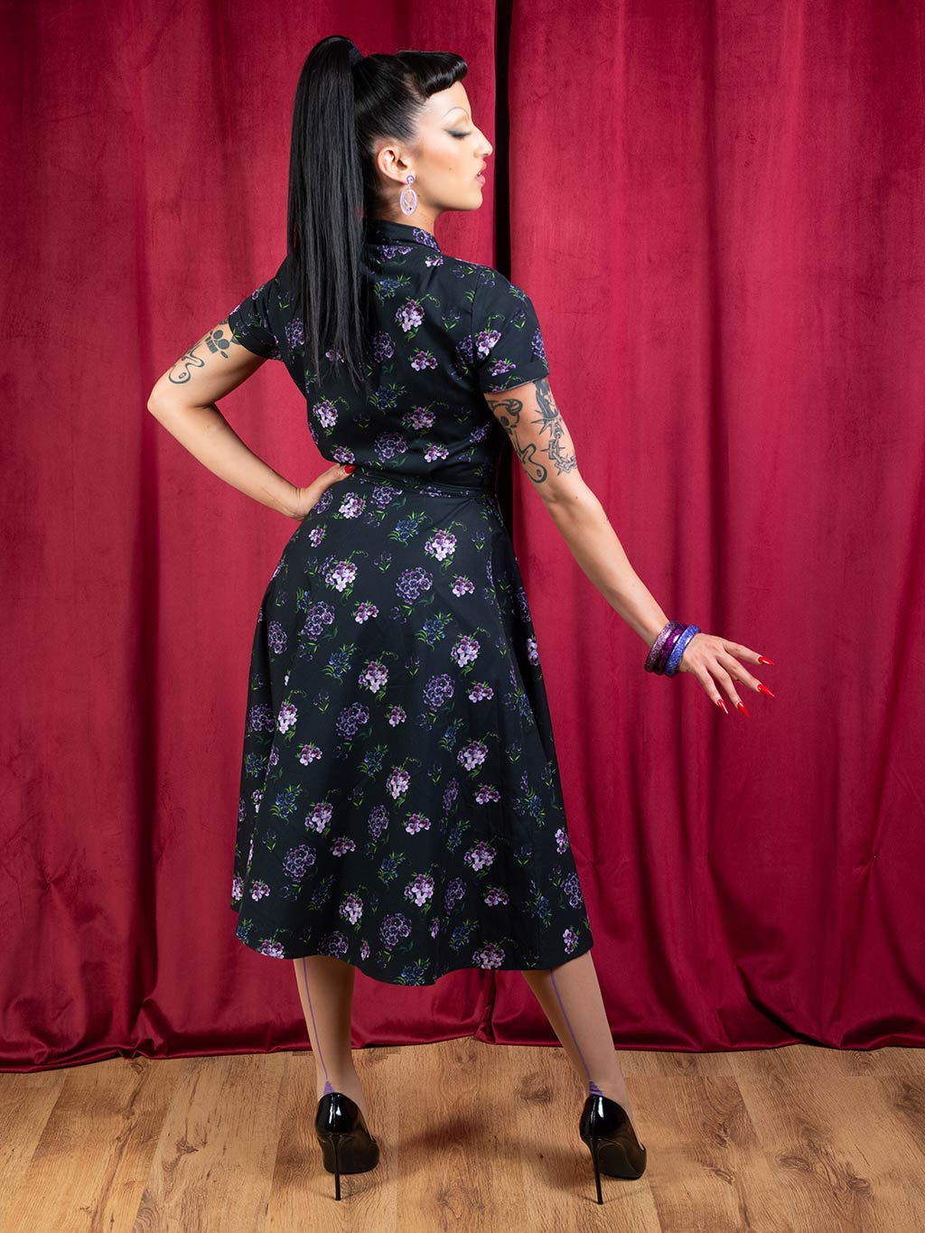 back view of a 1950s purple and black floral print shirtwaist dress worn with purple seamed stockings