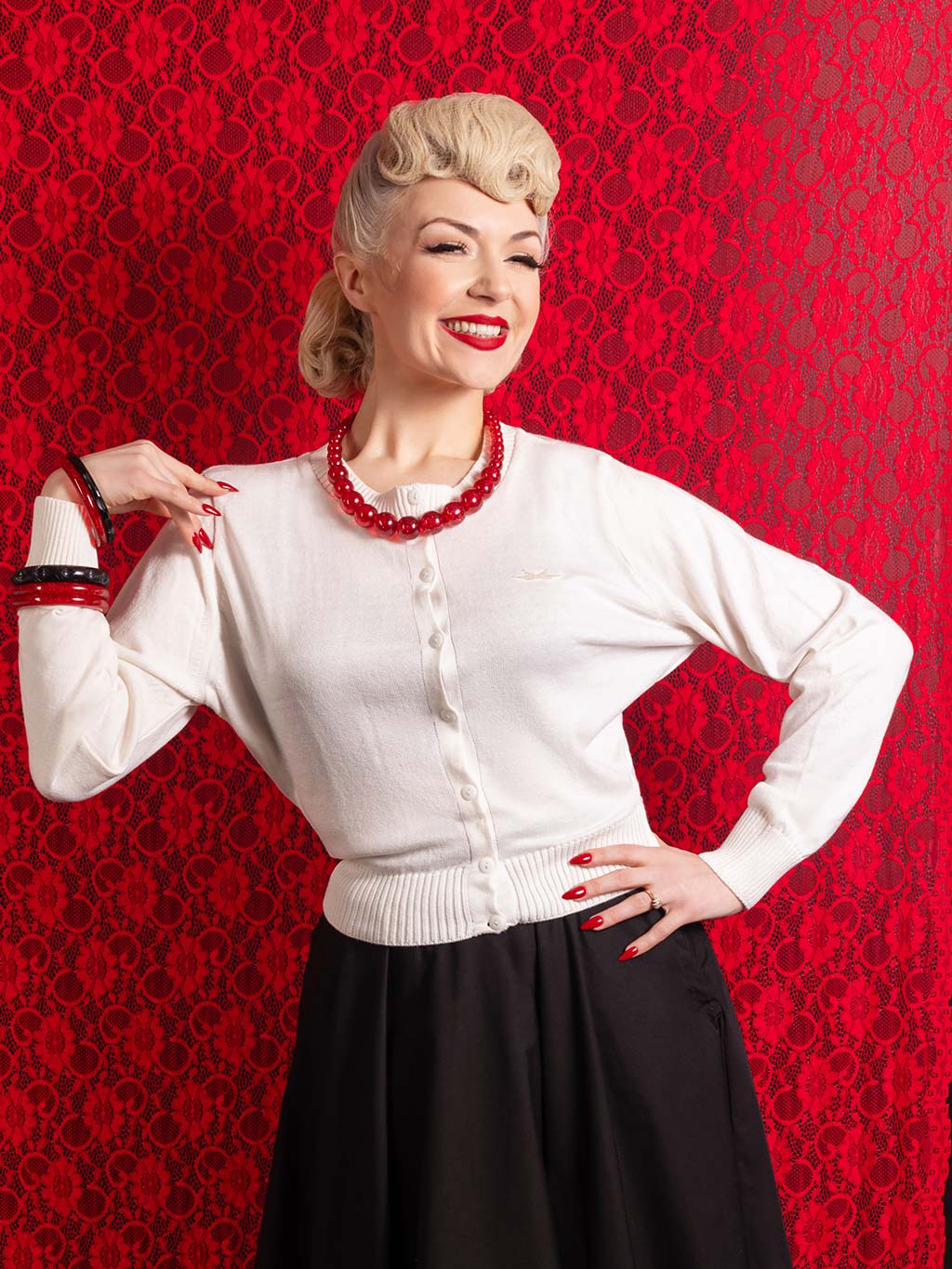 white waist length cardigan with a round neck, worn with black 1950s circle skirt and red retro glitter jewellery
