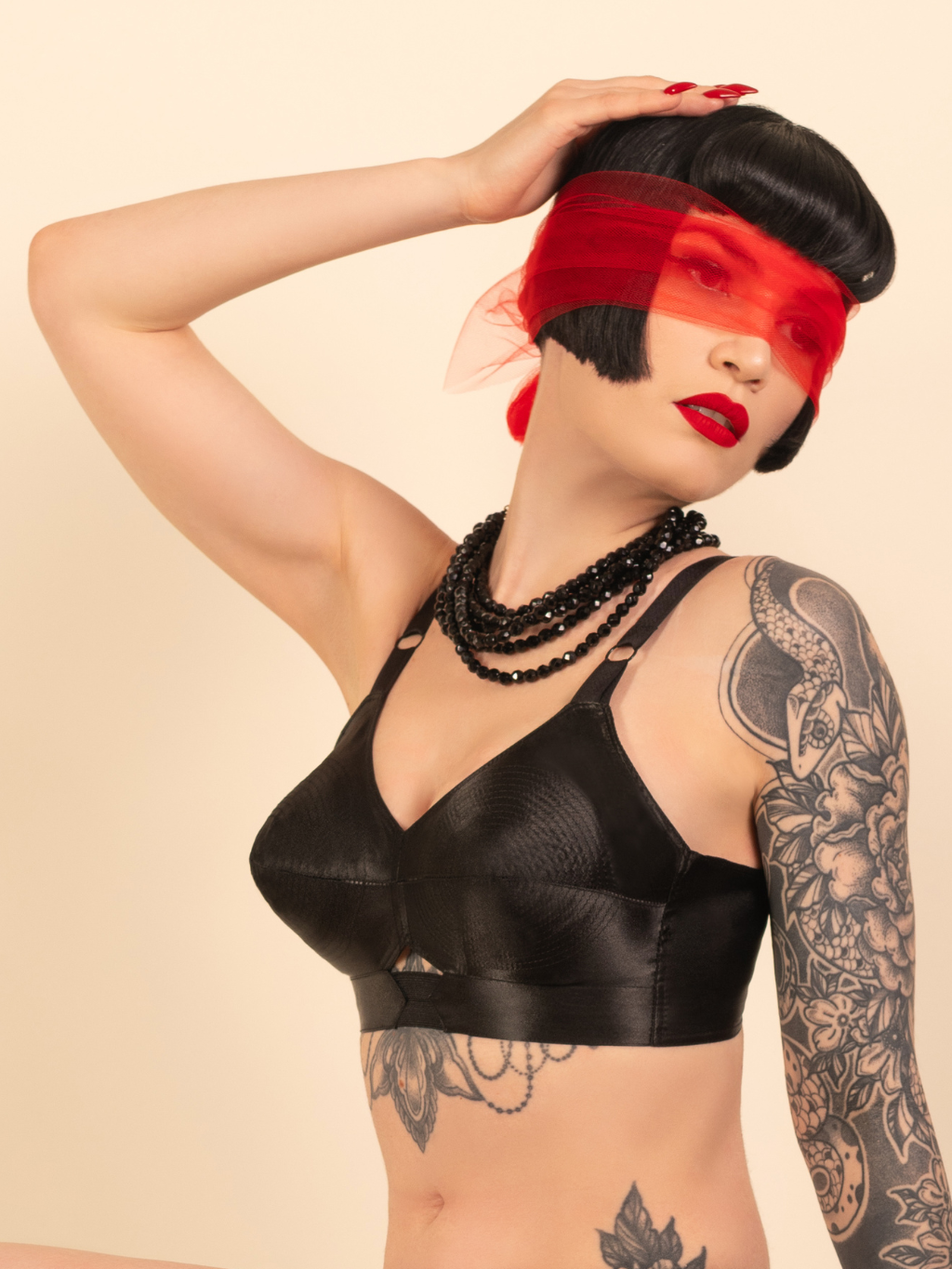 Woman wearing a black bra with tattoos on arms and neck, against a beige background