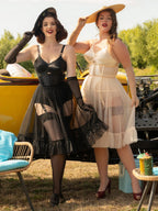 Two women in vintage 1950s frilly petticoats standing next to a yellow car with a scenic background.
