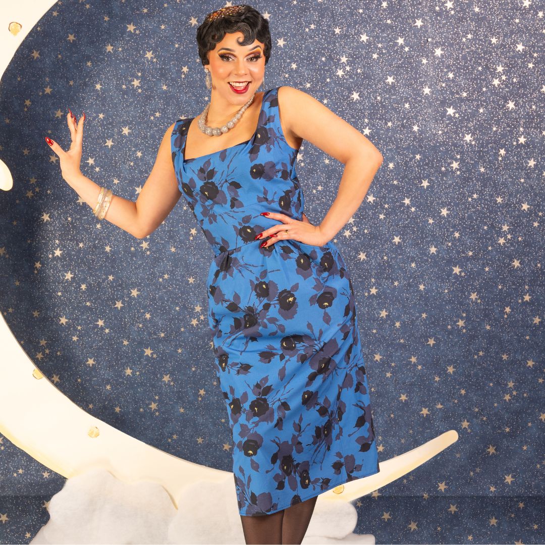 Woman in a blue dress with black floral print posing against a starry background