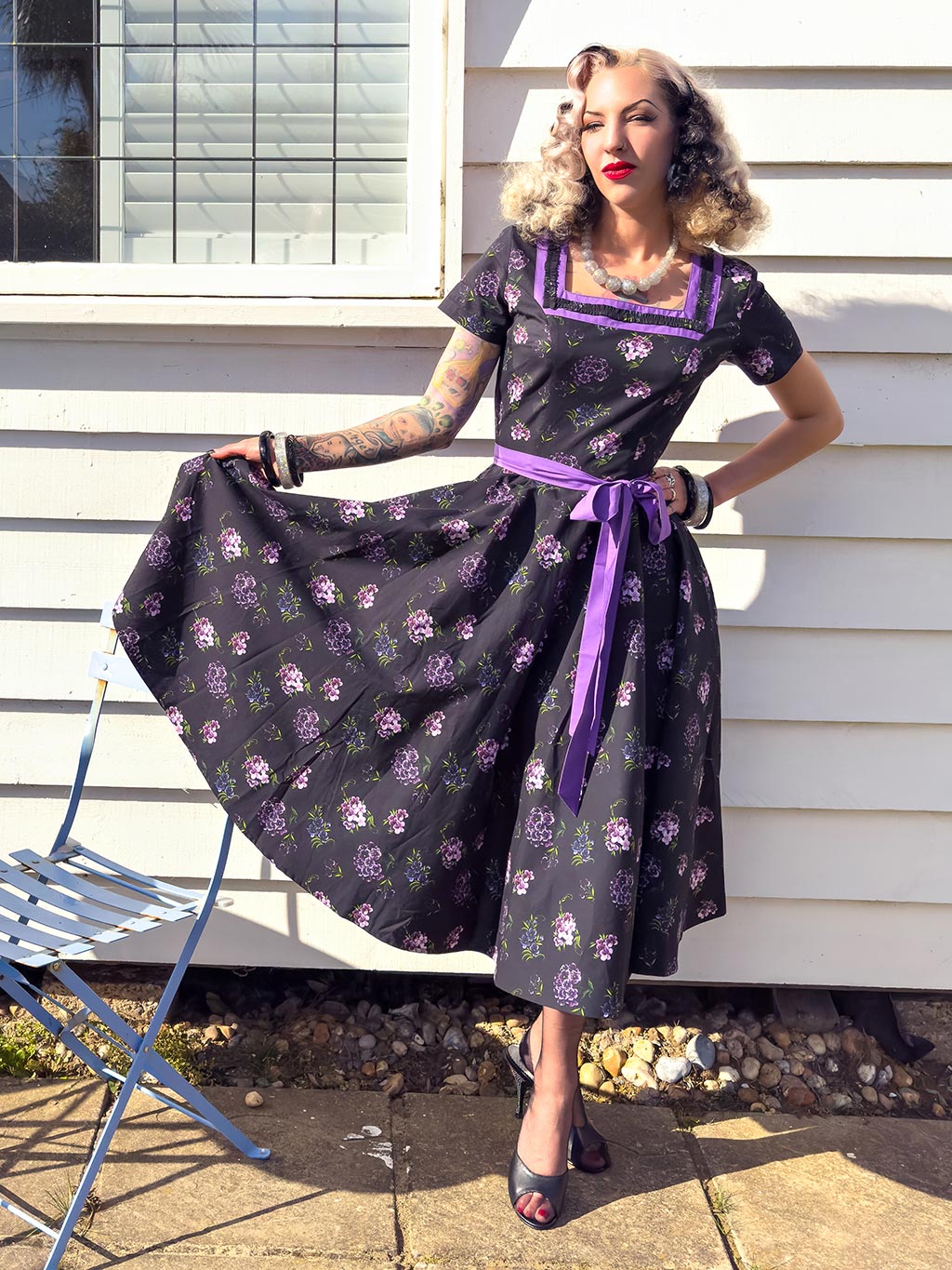 1950s purple floral dress with a square neckline and short sleeves worn with black seamed stockings