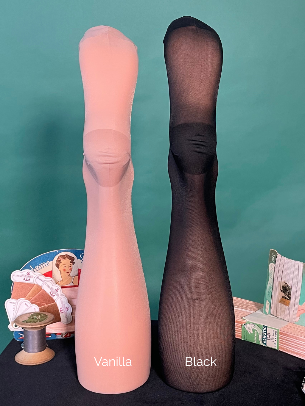 Two pairs of rht stockings, one vanilla and one black, on a green background with vintage-style spools of thread.