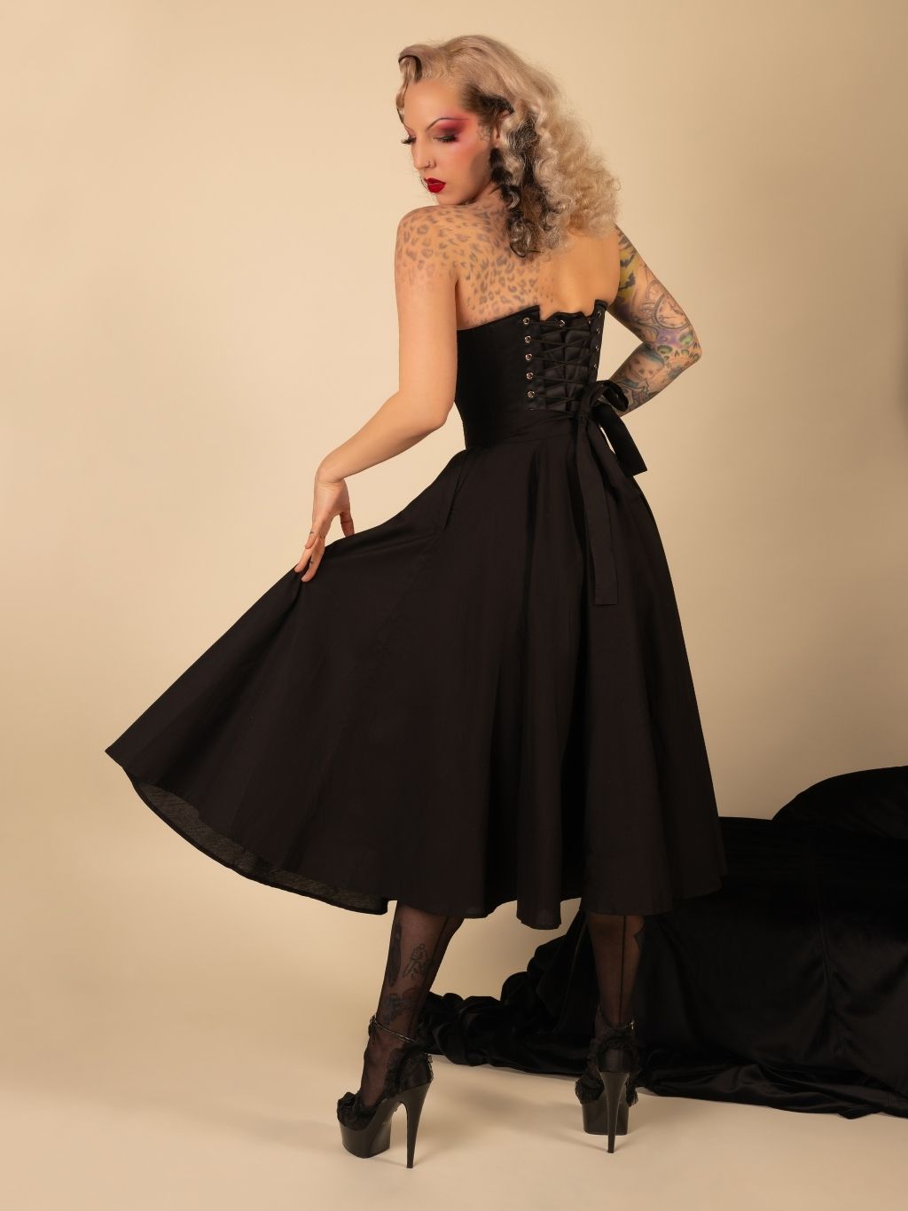 Woman wearing a  black skirt and corset  against a beige background