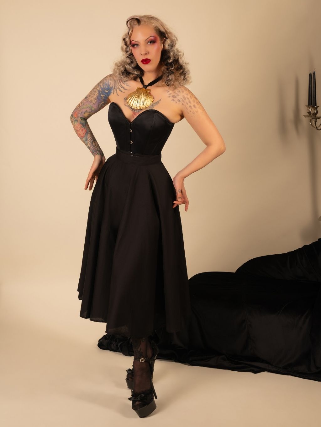 Woman in a black skirt and corset posing against a beige background