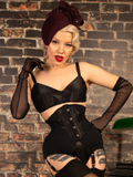 Woman in a black corset and headpiece against a brick wall