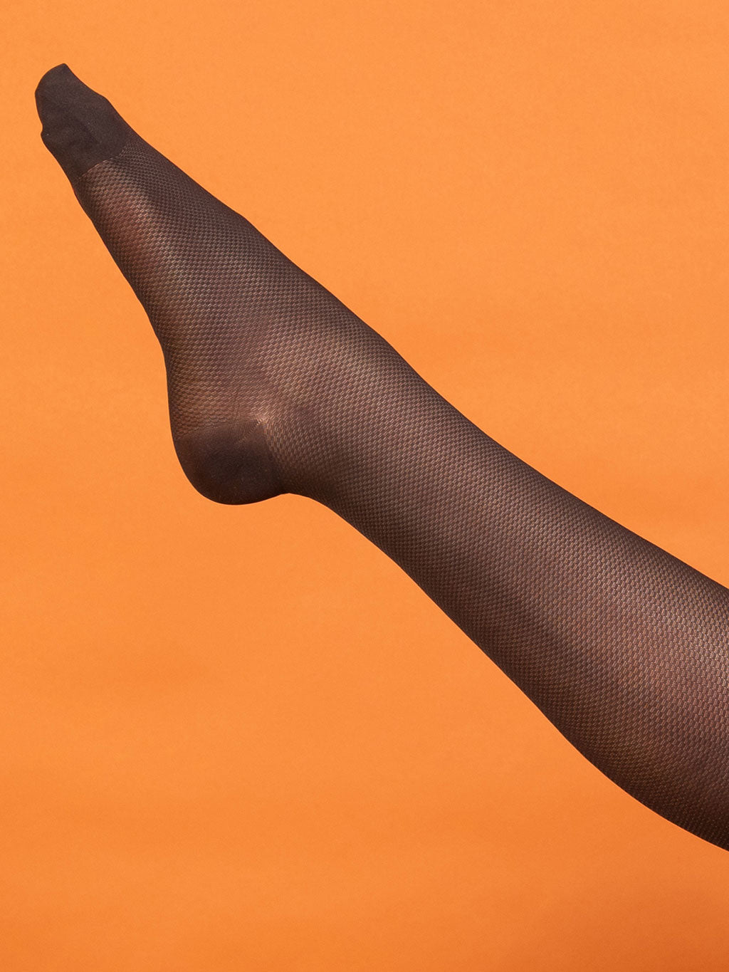 Black mesh rht tights on a person's leg against an orange background