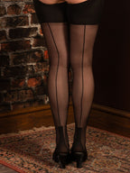 Person wearing black cuban heel stockings and high heels in front of a brick wall.
