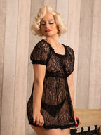 Woman wearing a black lace baby doll against a wooden paneled wall.
