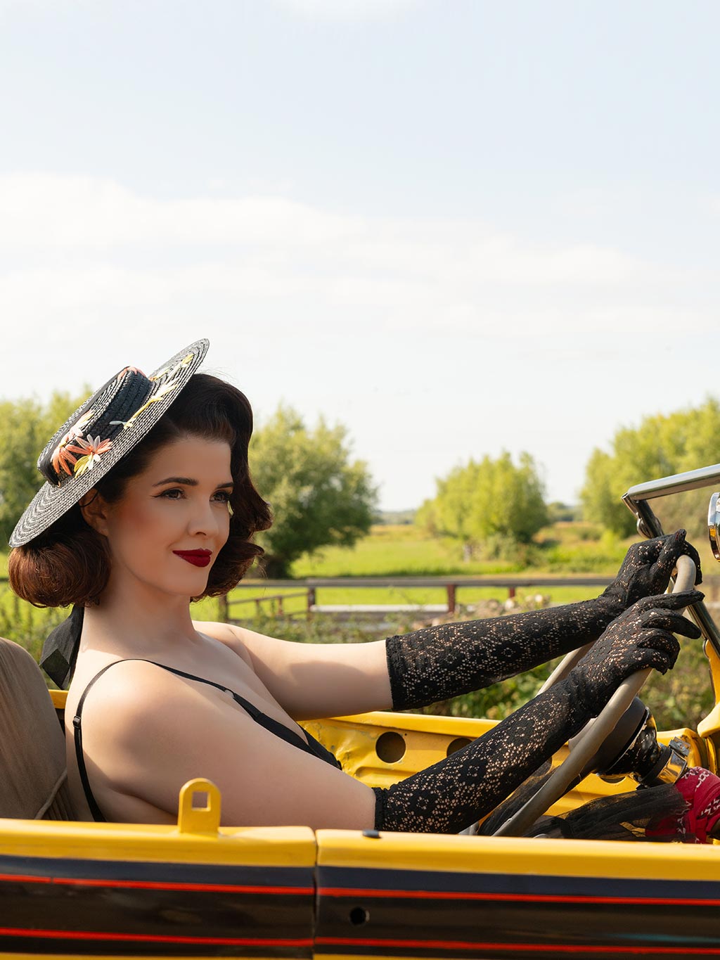 Woman driving a vintage car with a scenic background wearing black lace gloves