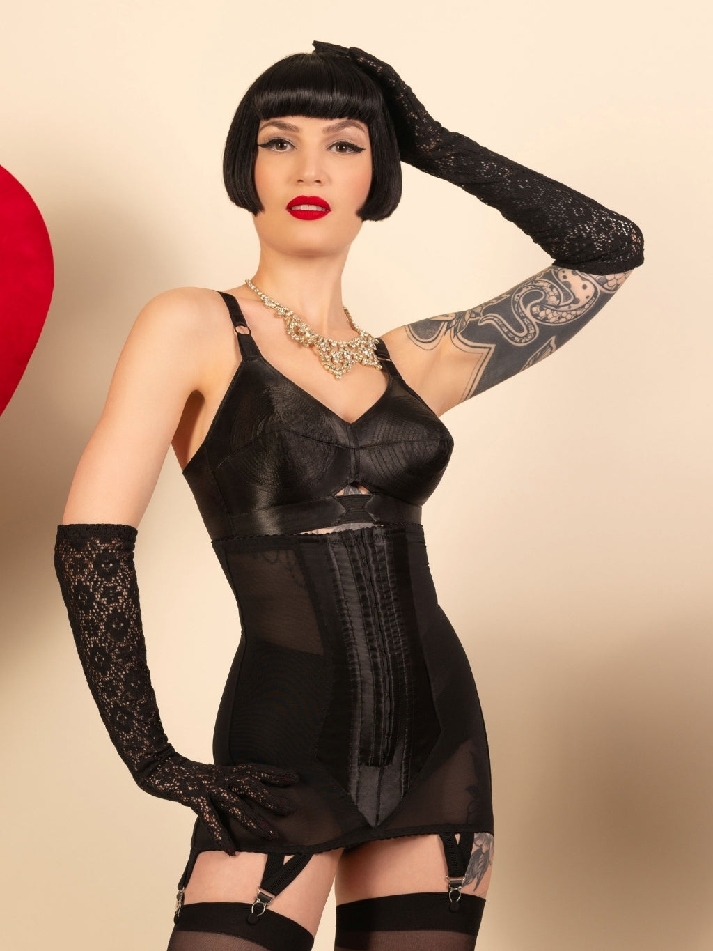 black lace cocktail gloves worn with a 1950s black bullet bra and girdle by a woman with a short black bob


