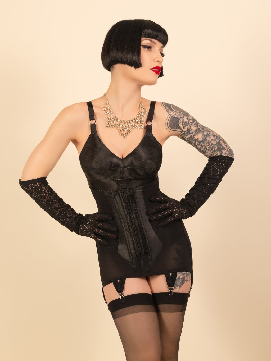 black lace cocktail gloves worn with a 1950s black bullet bra and girdle by a woman with a short black bob and red lipstick