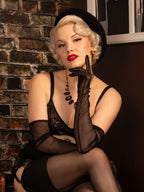 Woman in long black gloves and vintage lingerie and black gloves posing against a brick wall.