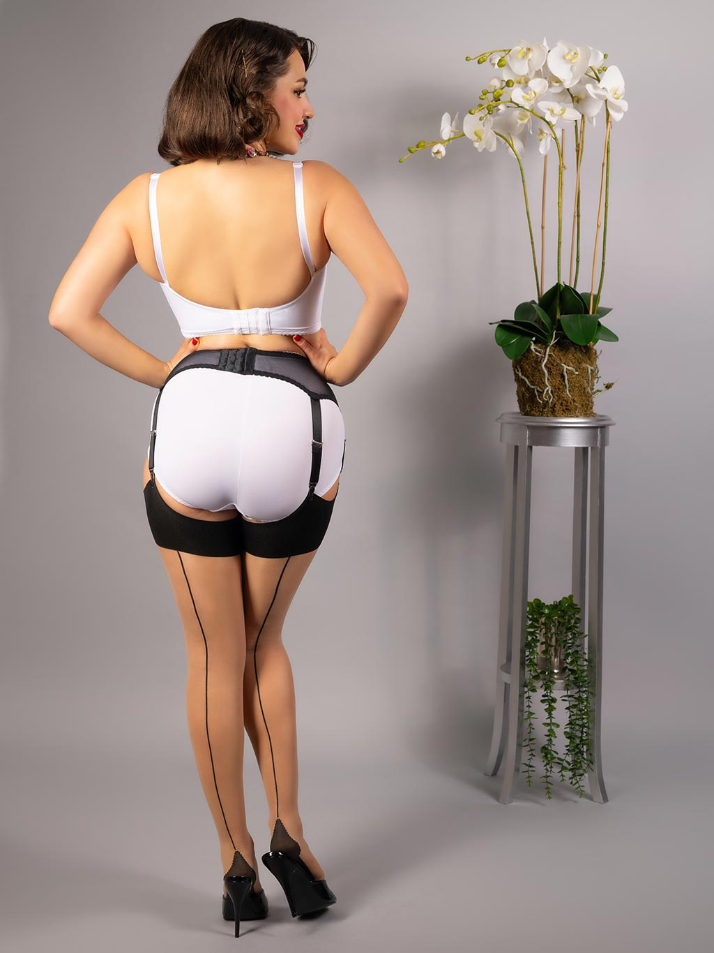 back view of black boned suspender belt worn with retro white lingerie and seamed stockings