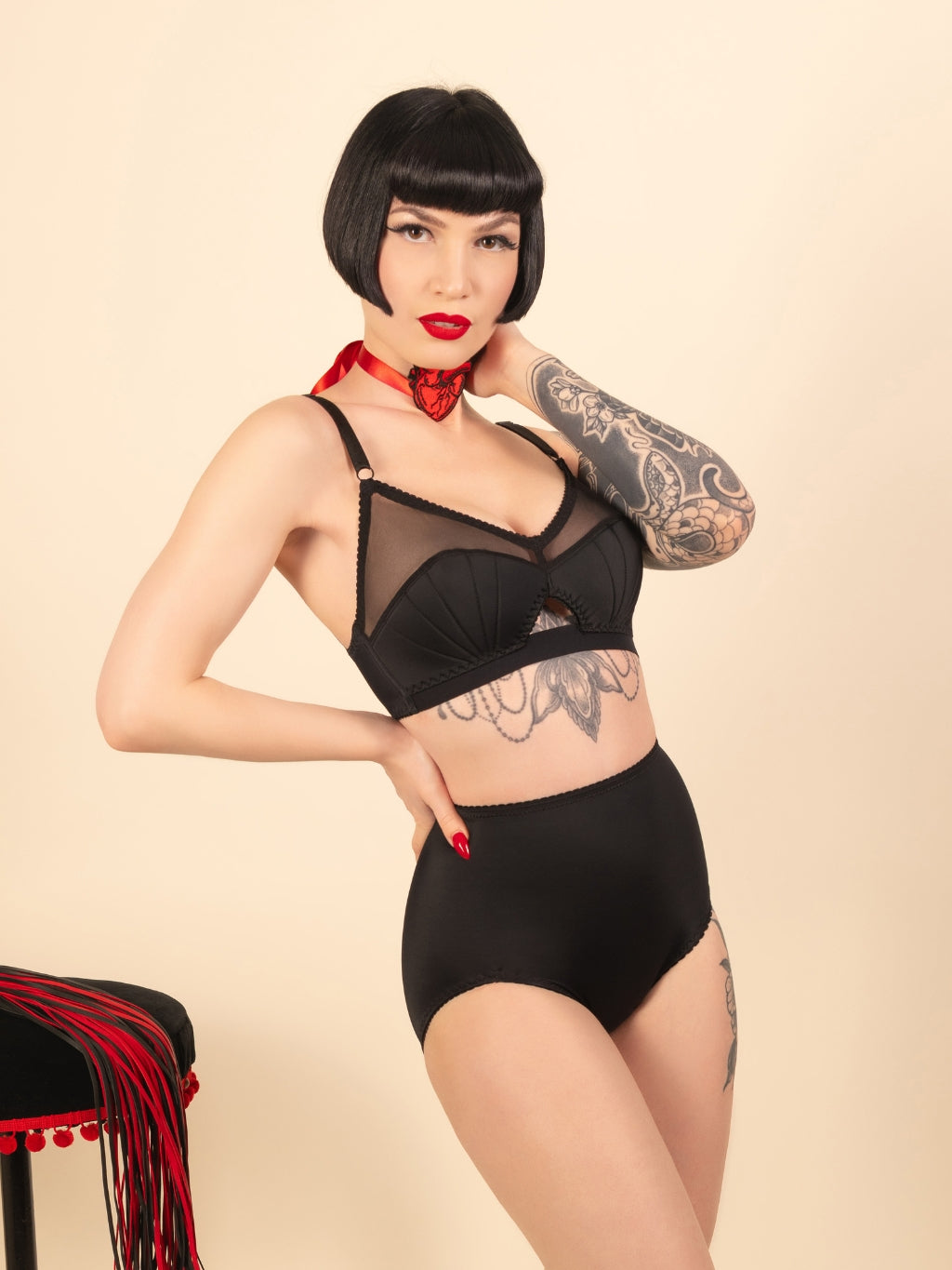 Woman wearing a black lingerie set with tattoos on a beige background