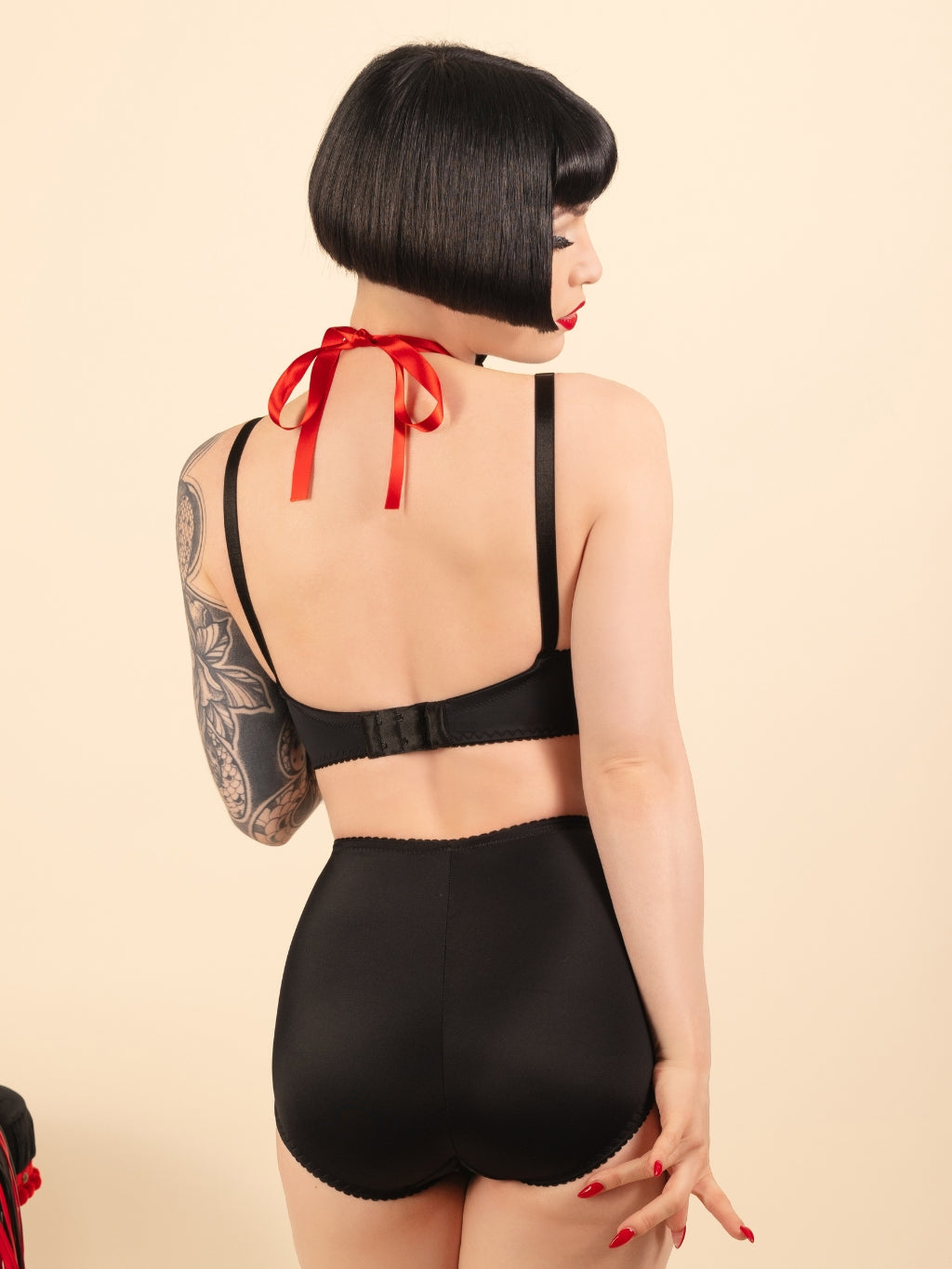 Woman wearing a black lingerie set with red accents on a beige background