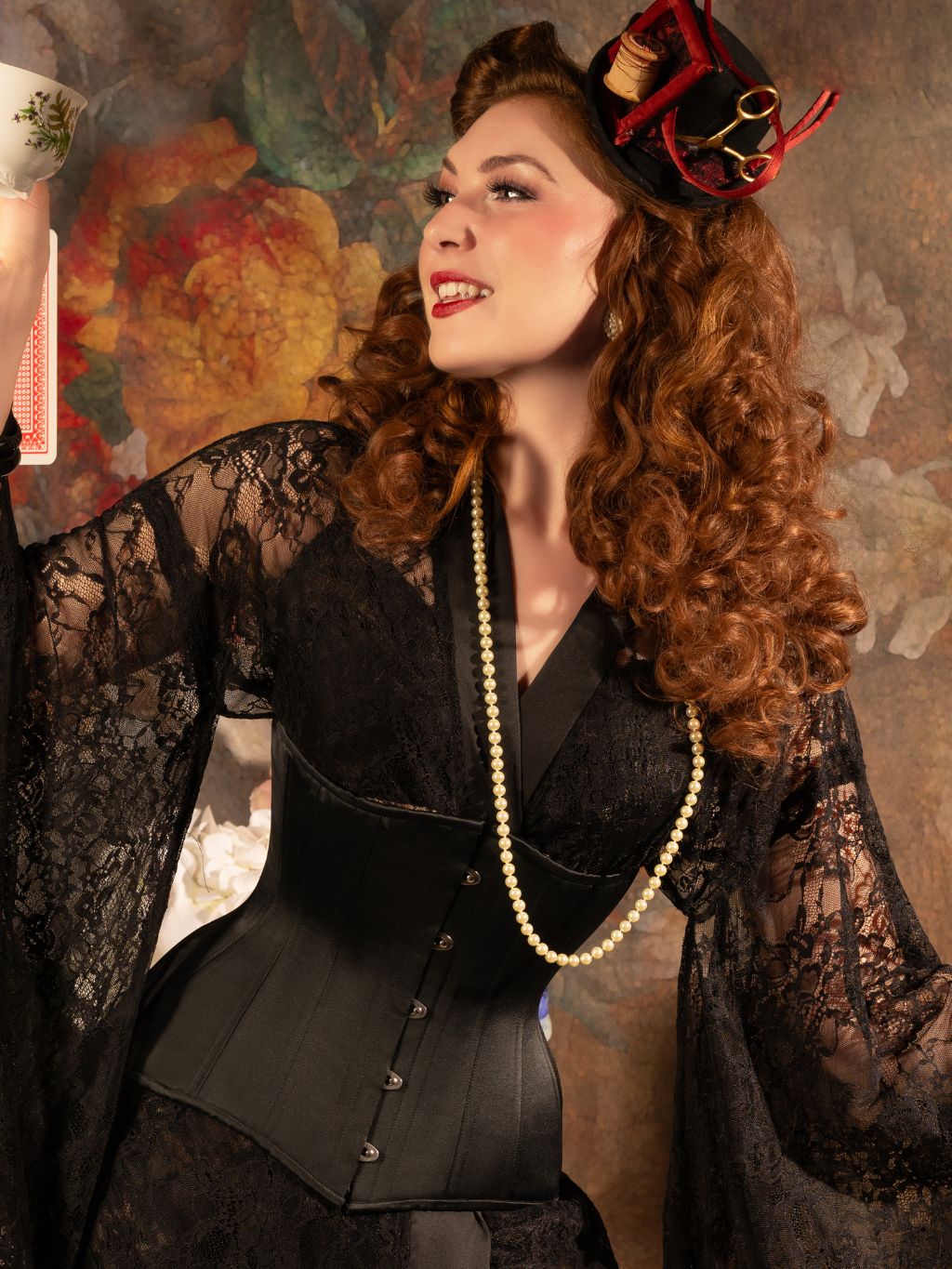 Woman in a black corset worn over a kimono with a decorative hat against a floral background