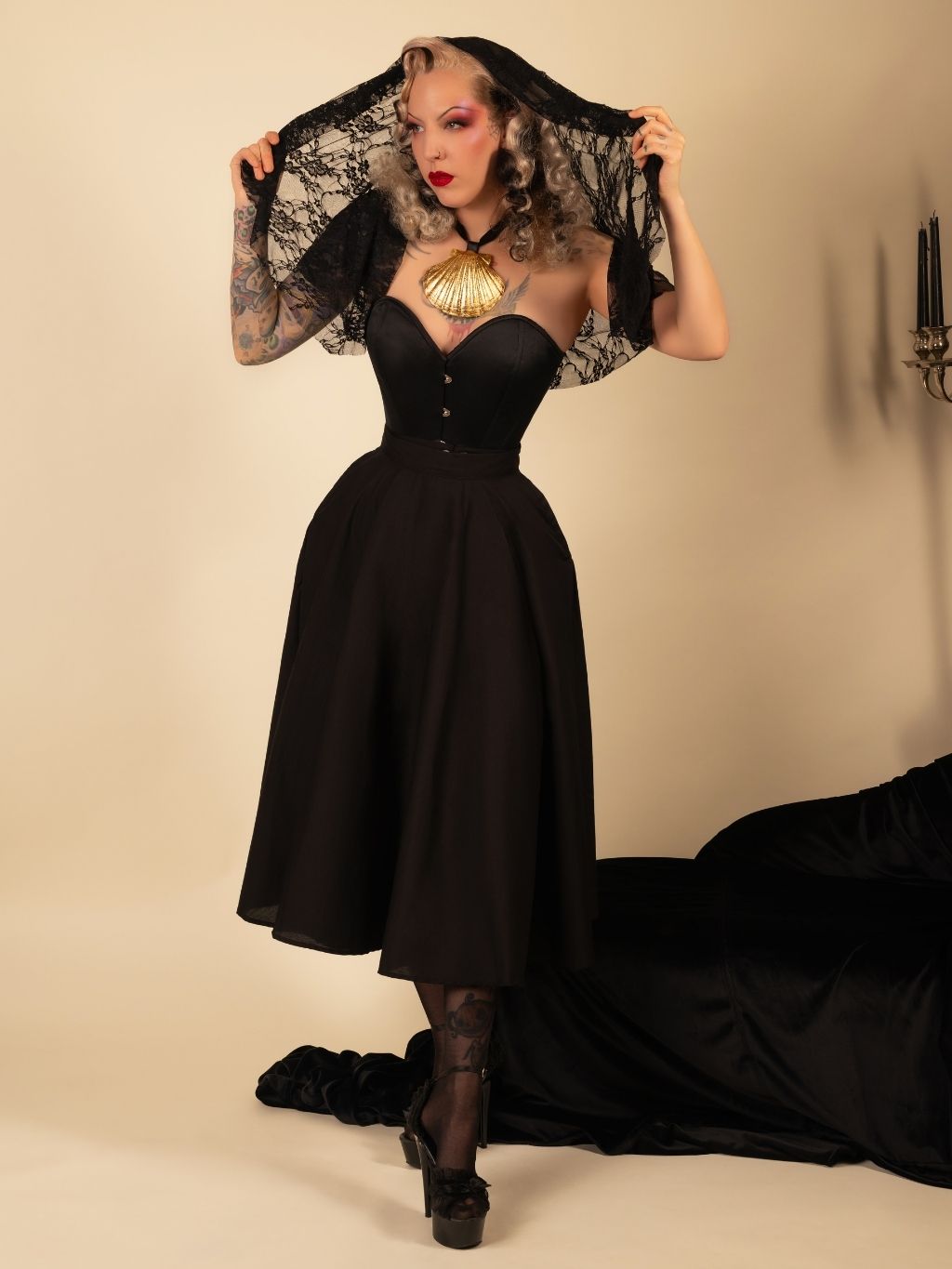 Woman wearing a black  circle skirt and corset with a lace shawl against a beige background
