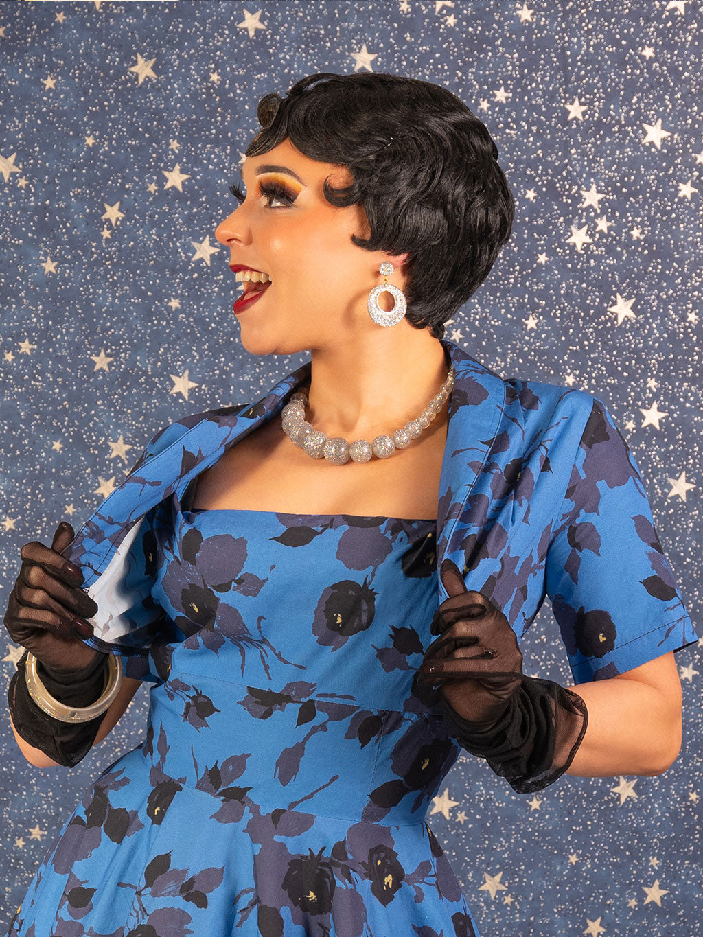 Woman in a blue floral dress with black gloves against a starry background