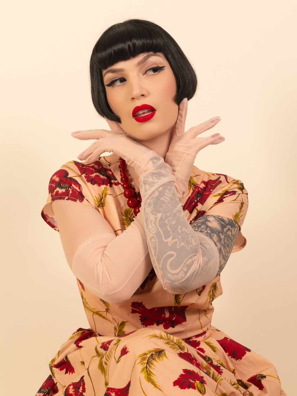Woman with tattoos wearing a floral dress and long pink gloves against a beige background