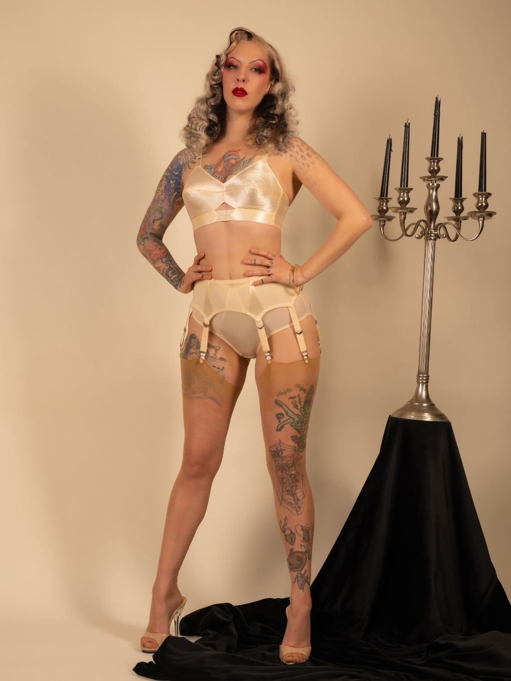 Woman in vintage-style lingerie posing next to a candelabra on a beige background