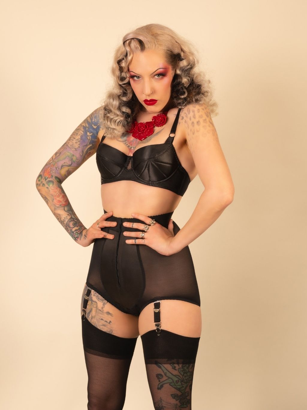Woman wearing a black lingerie set with tattoos and red hair against a beige background