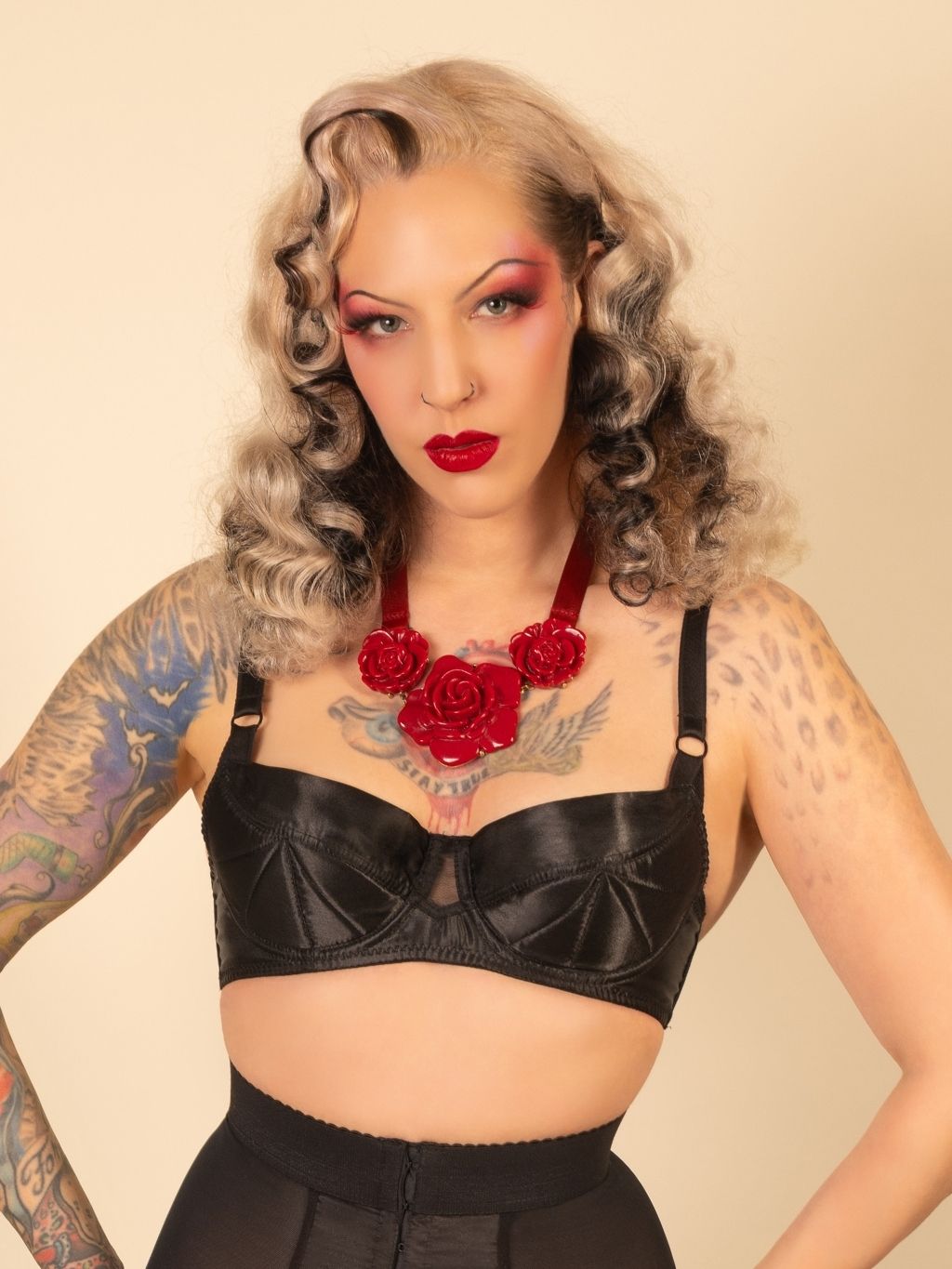 Woman wearing a black bralette with red floral accessories against a beige background
