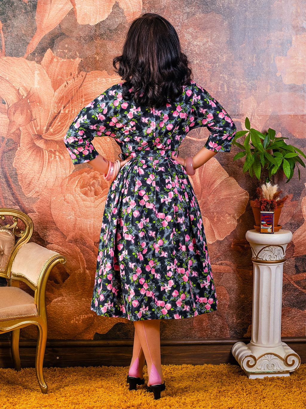 back view of grey and pink floral 1950s dress with belt and bracelet length raglan sleeves worn with pink seamed stockings and matching pink bangles