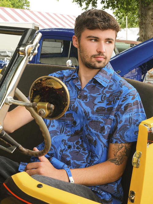Man sitting inside a vintage vehicle with a blue shirt and tattooed arm.