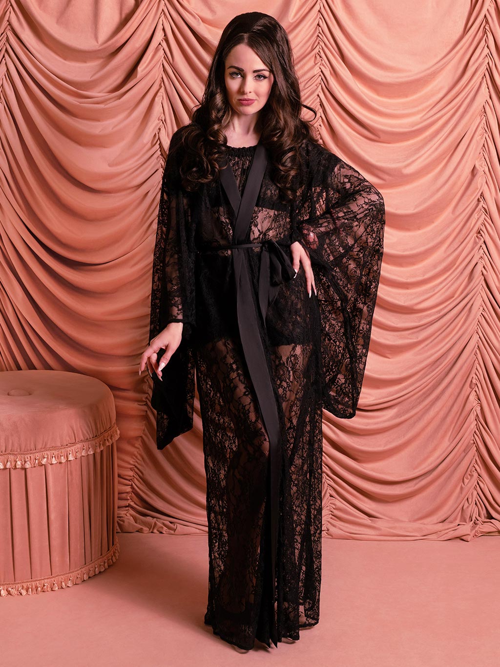 Front view of long black lace kimono on 1960s-inspired model with Priscilla Presley-style dark hair in pink boudoir setting.