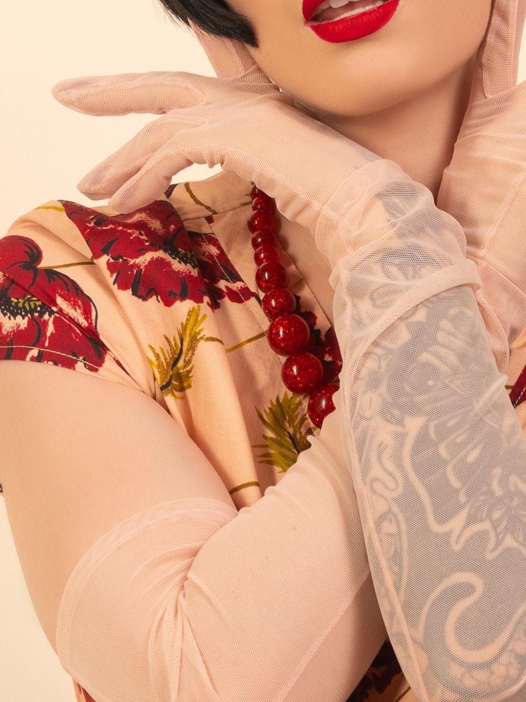 Person wearing a floral dress with red berries and sheer pink gloves, against a beige background.