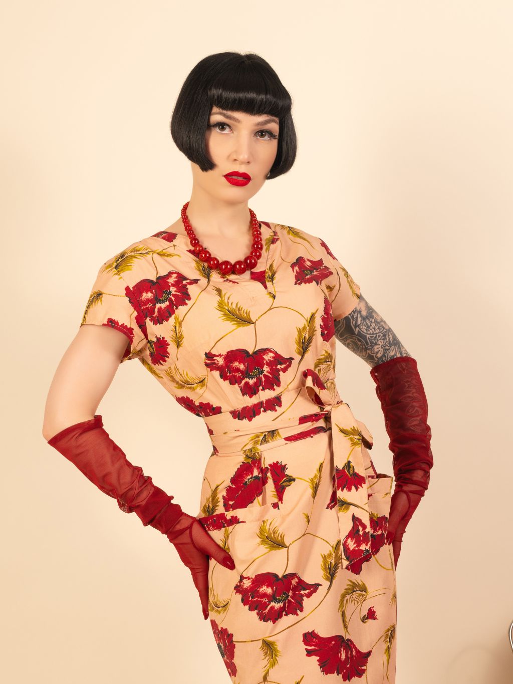 Woman wearing a floral dress with red flowers, red gloves, and a necklace on a beige background