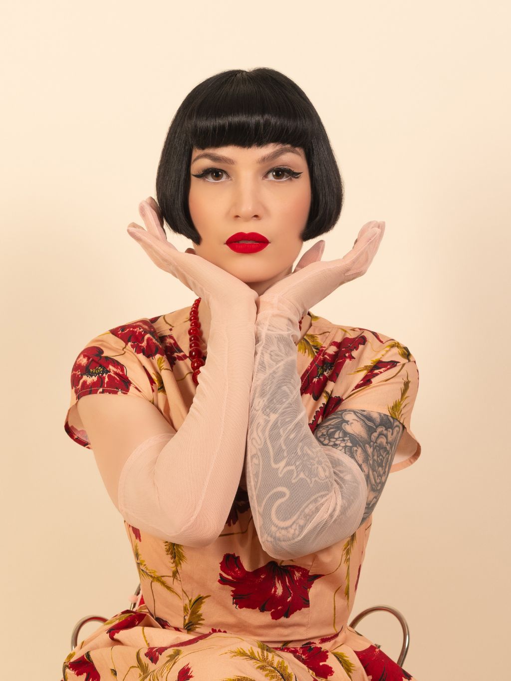 Woman with a floral dress and long pink mesh gloves against a beige background