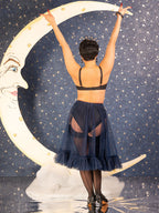 Person in a vintage navy blue frilly petticoat and lingeriet standing against a starry night sky with a crescent moon.
