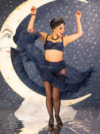 Woman in a vintage navy blue frilly petticoat and lingerie dancing against a celestial background with a face on the moon.