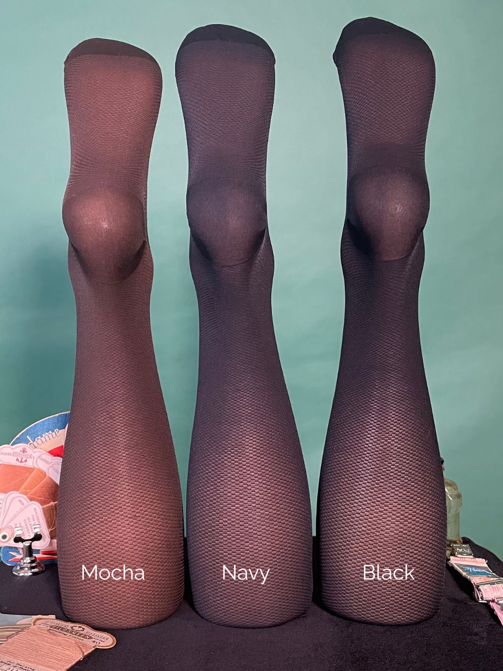 Three pairs of tights in Mocha, Navy, and Black on a table with a light blue background.
