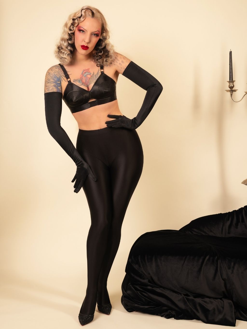 Woman in a black outfit with long gloves posing against a beige background