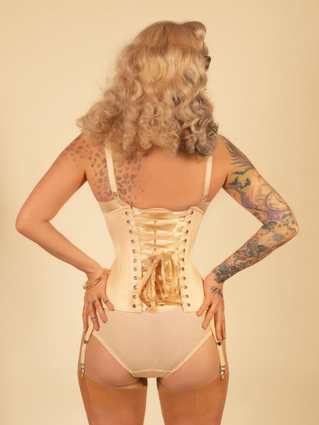 Woman wearing a beige corset and thong against a beige background