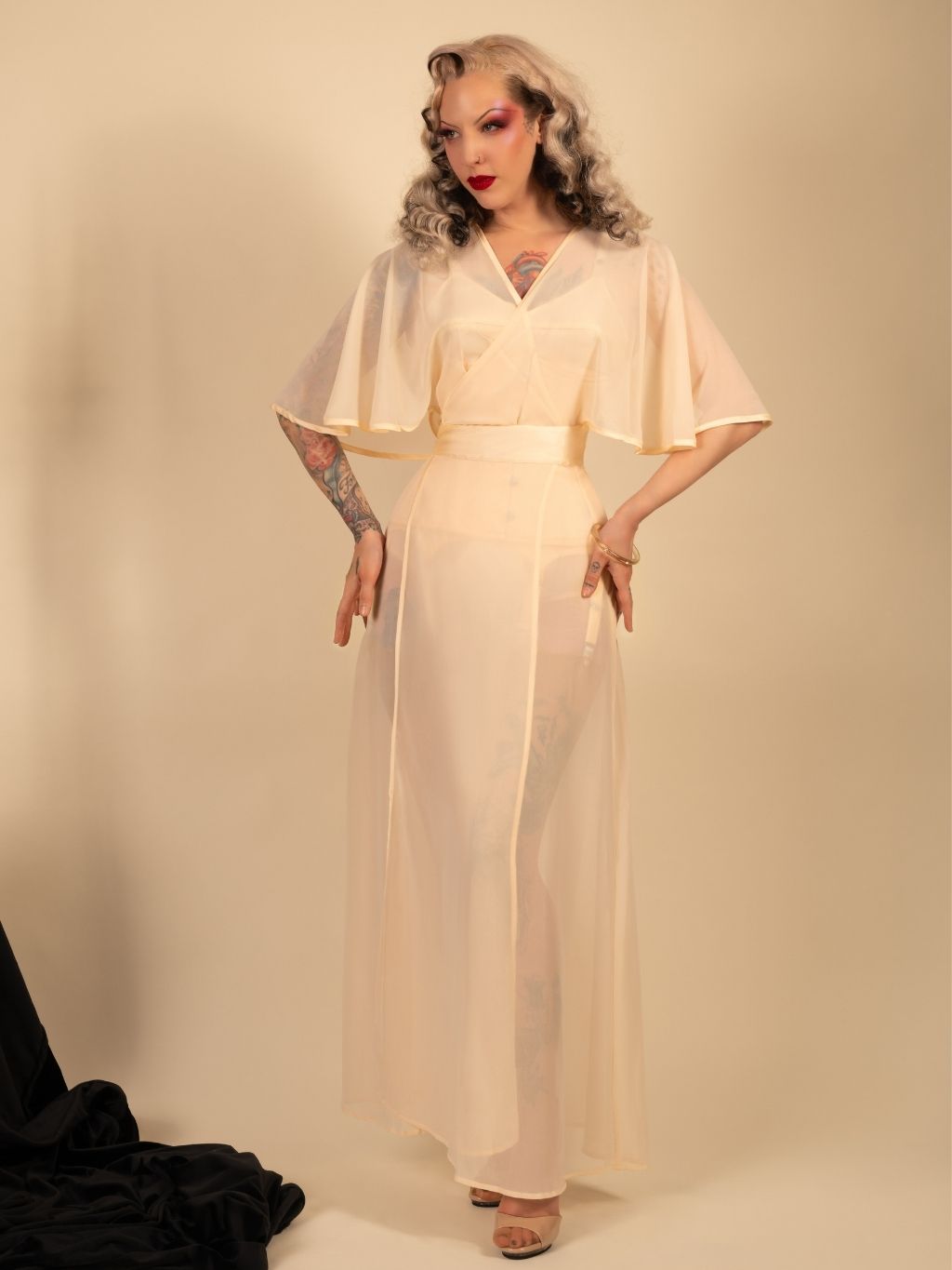 Woman wearing a long, light-colored  robe with cape sleeves against a plain background