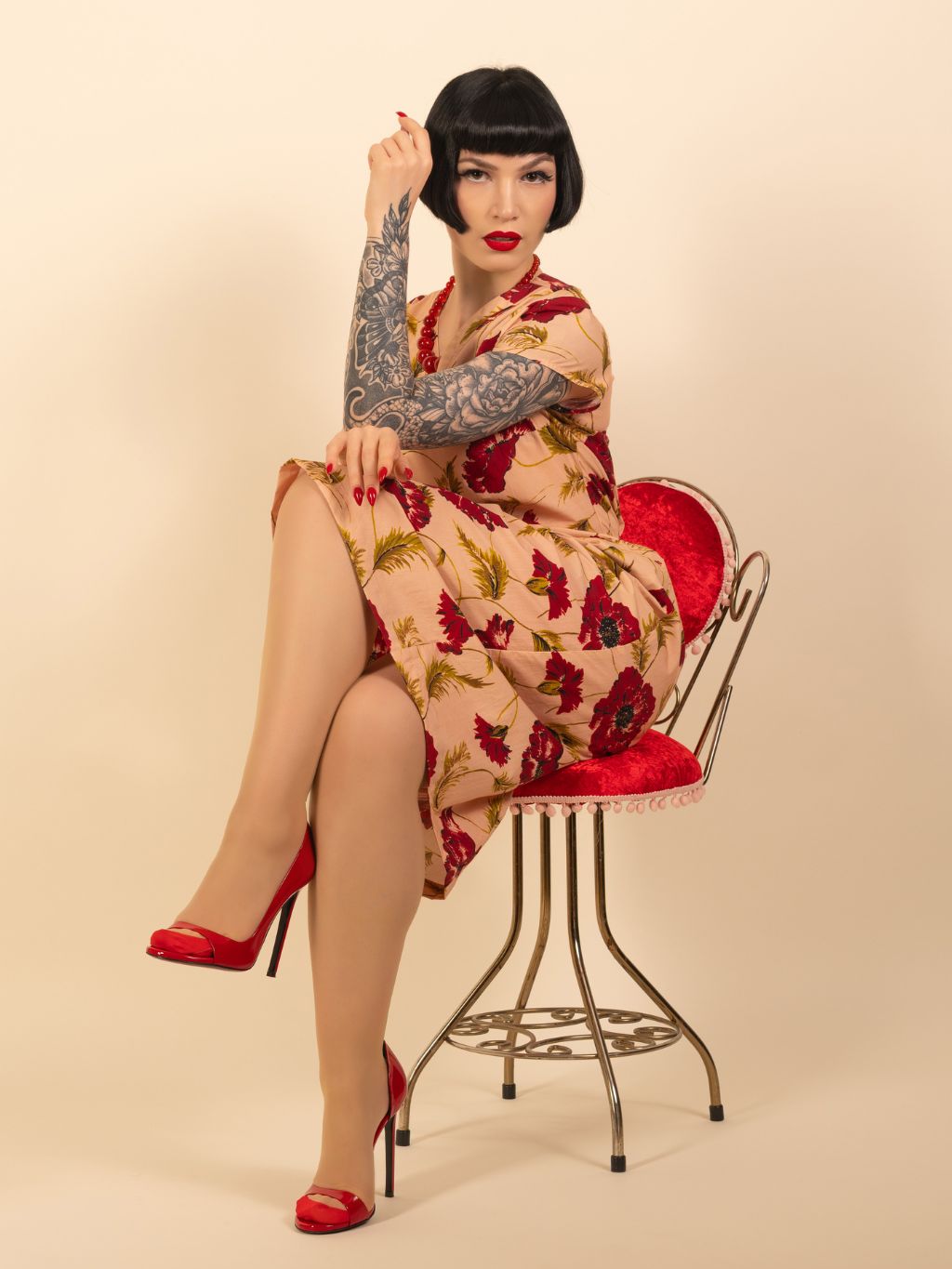 Woman in a floral dress sitting on a chair against a beige background