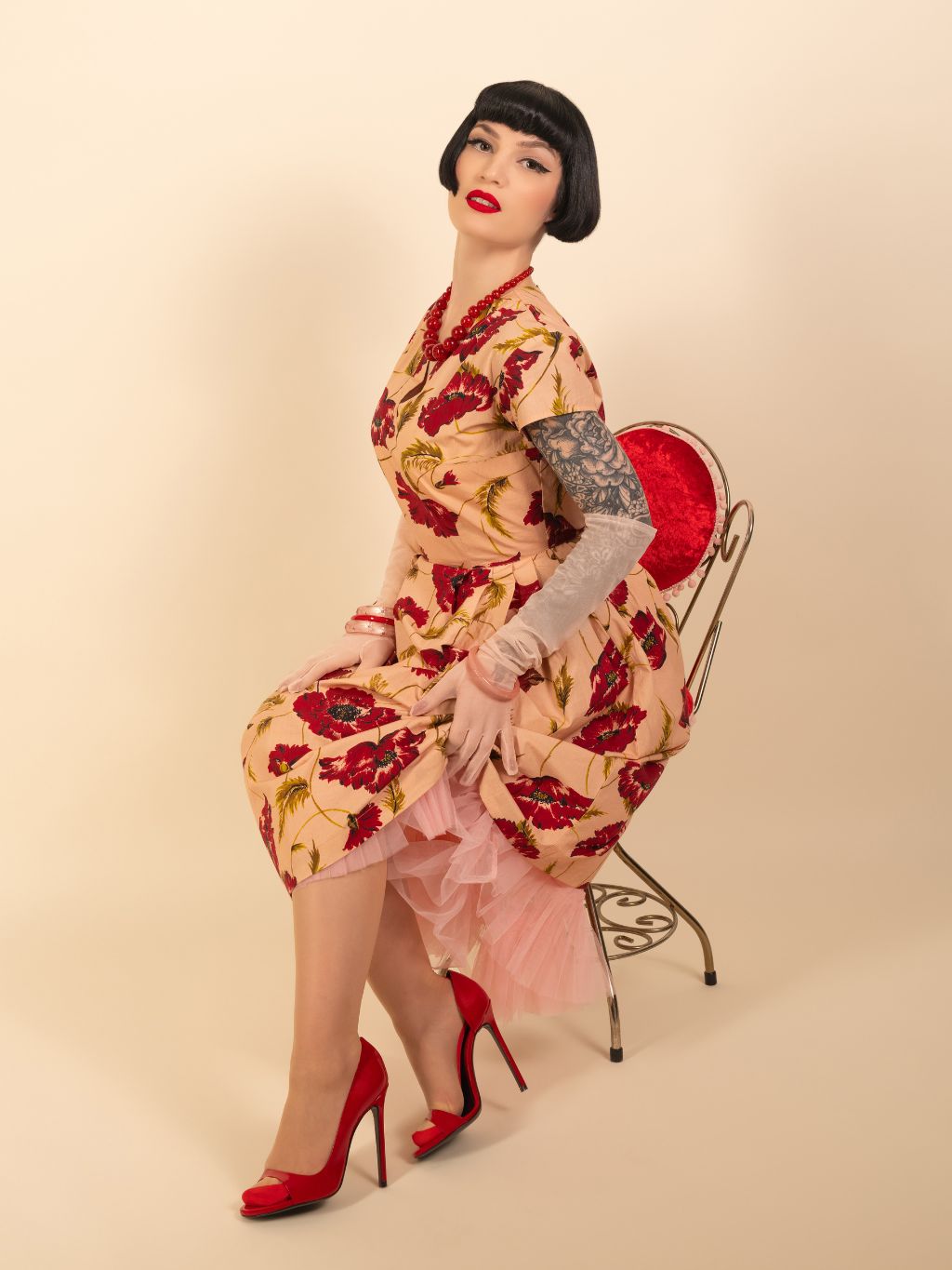 Woman in a floral dress sitting on a chair against a beige background