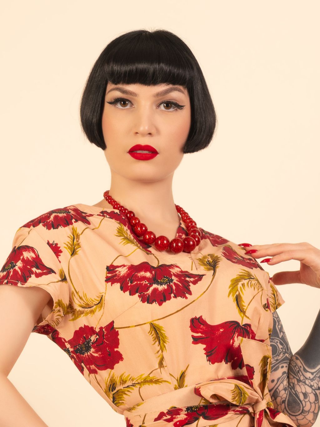 Woman wearing a floral dress with red flowers and a red necklace against a beige background
