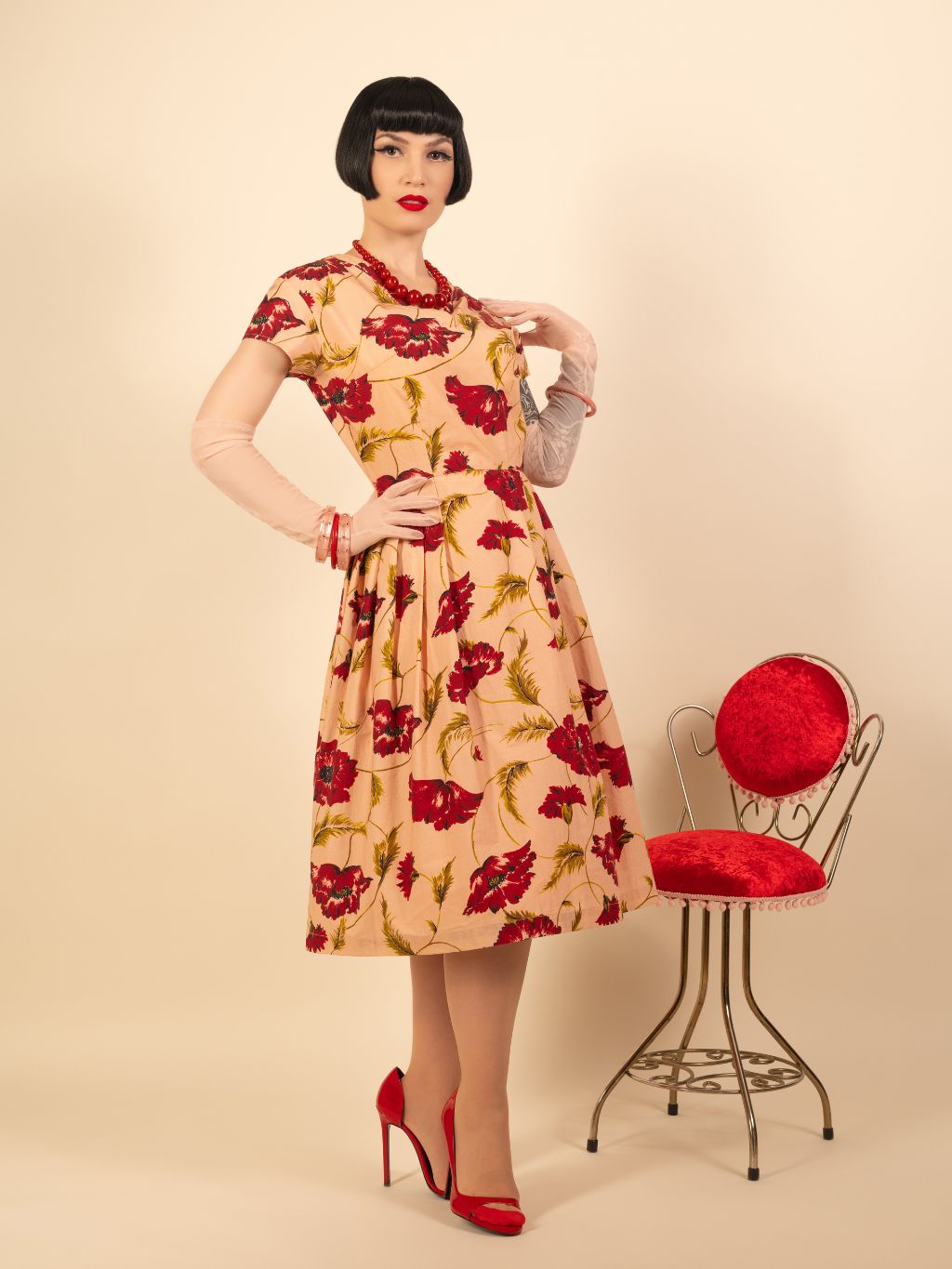 Woman wearing a floral dress with a red chair on a beige background