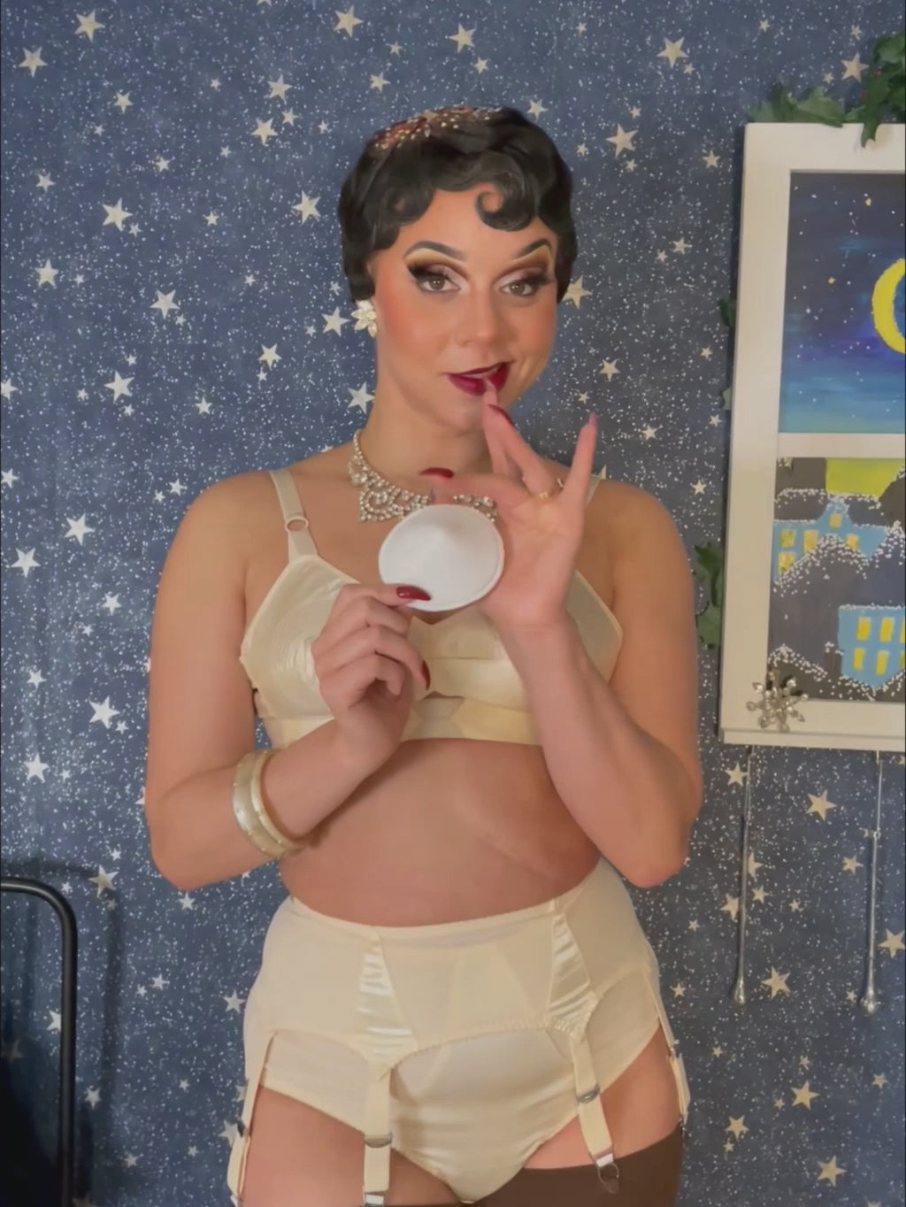 video of woman in a peach satin bullet bra holding white bullet bra pads against a starry background