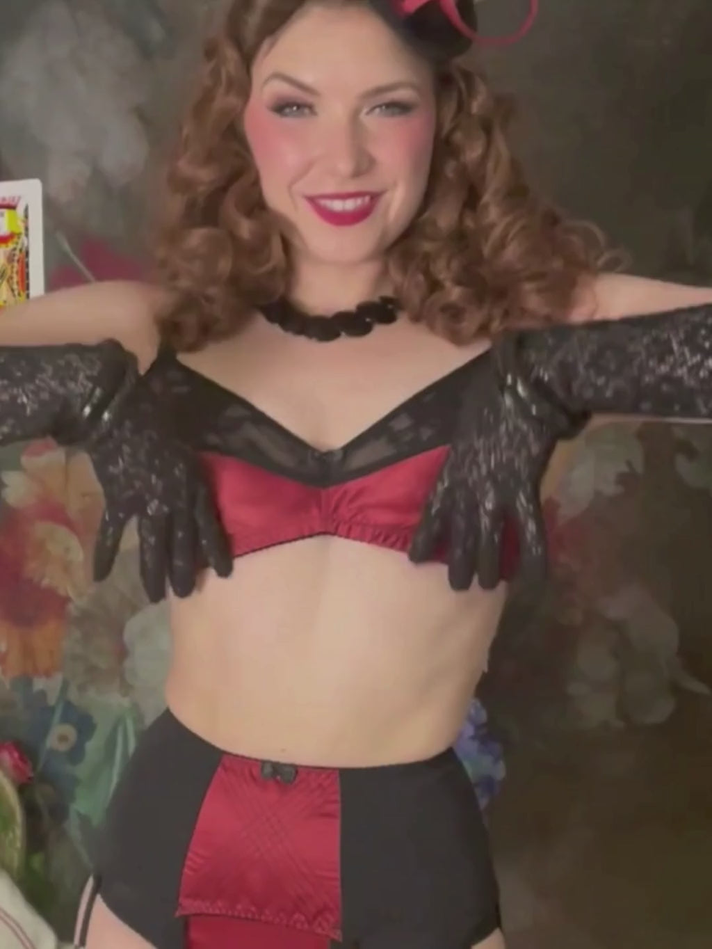 Woman wearing a black lingerie set with a decorative hat against a floral background