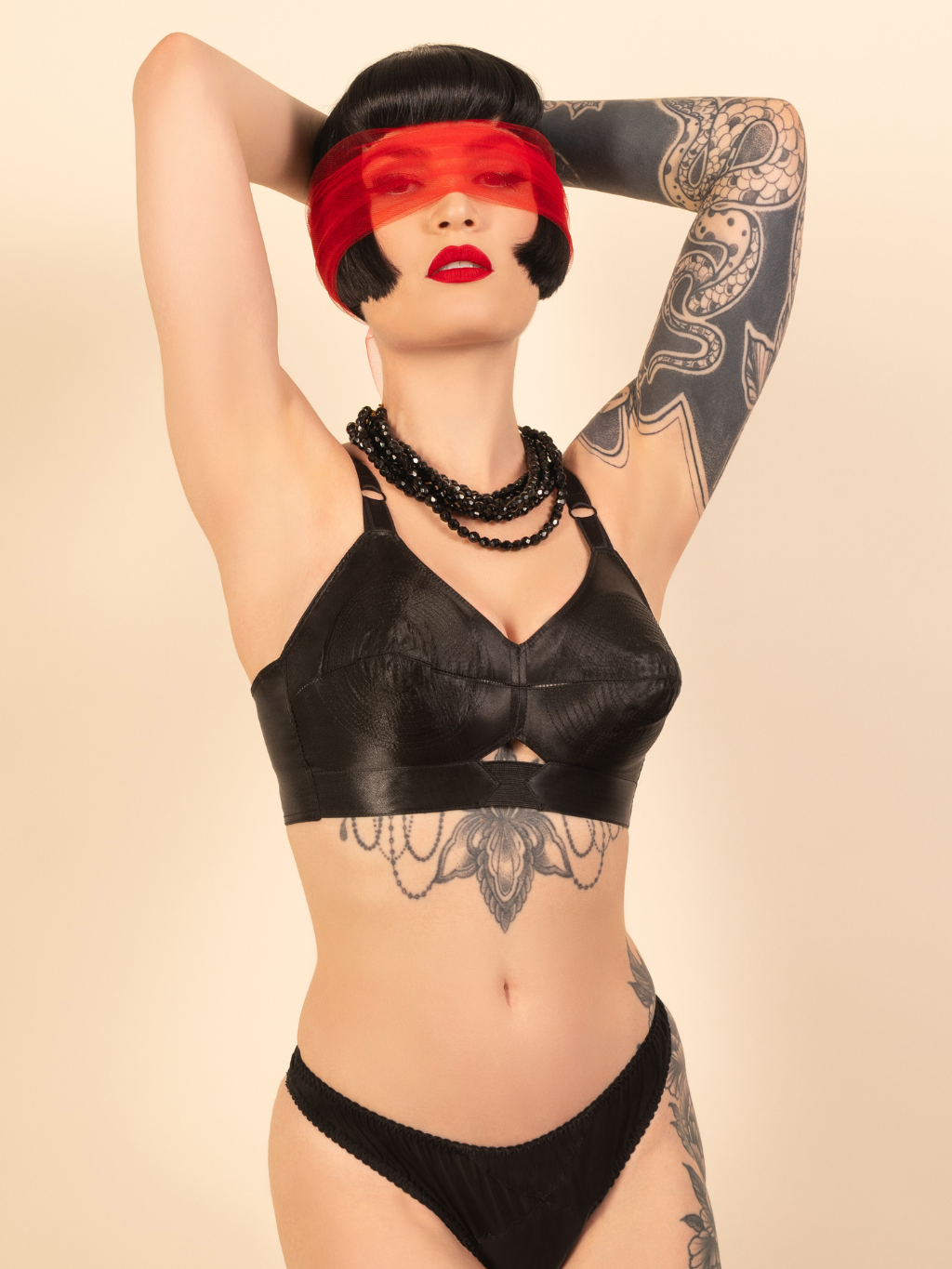 Woman wearing a black bra with tattoos on arms and neck, against a beige background