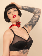 Woman wearing a black bralette with tattoos and red lipstick against a beige background