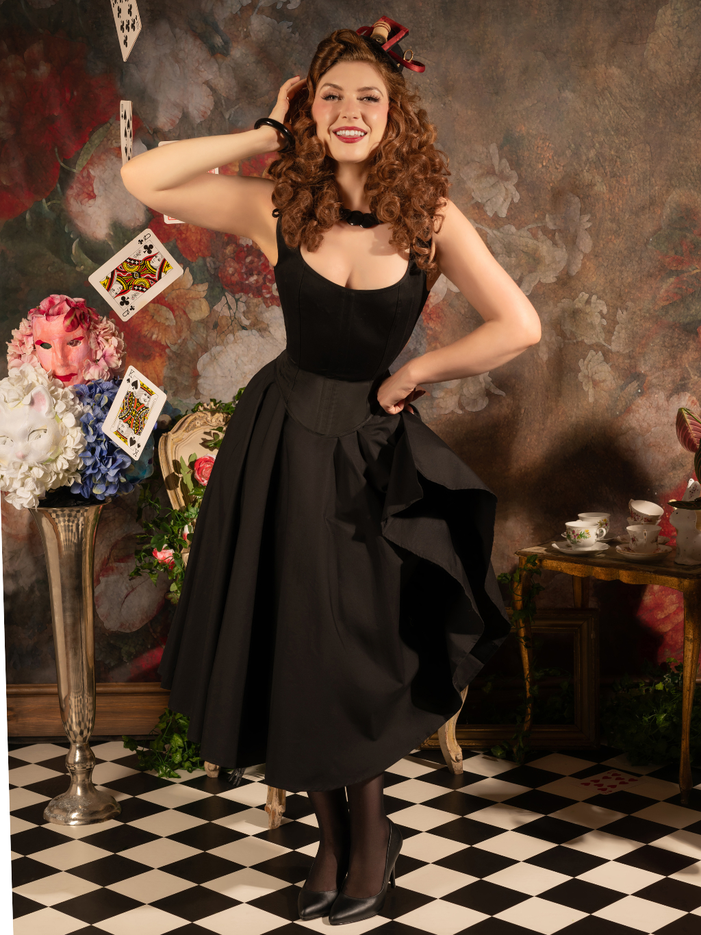 Woman in a black dress posing in a room with checkered floor and decorative elements.