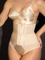 Woman wearing a peach satin waist cincher against a dark background