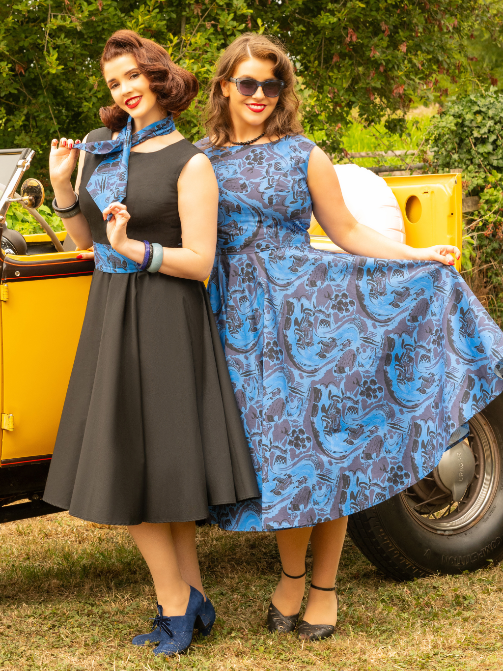 Woman in a blue dress posing next to a vintage car with greenery in the background
